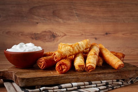 Fried spring rolls with cheese, on a wooden chopping board, with cream sauce, no people