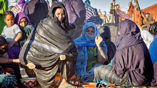 Gathering of people in colourful, traditional clothing in a desert landscape, woman at the