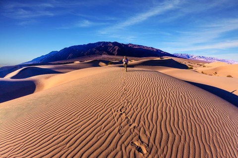 Sunrise in the orange sands of the desert Mesquite Flat, USA. Woman - photographer is among the