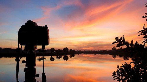 Silhouette of a camera at sunset.Dslr camera shooting on a cityscape sunset with lake reflection