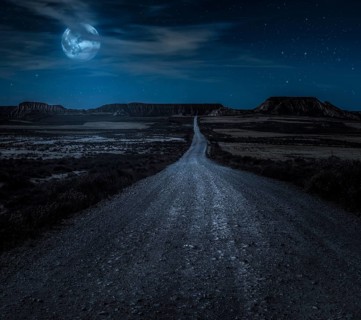 Moon, stars and clouds in the night. Wild west road illuminated from the moon. Moonlight and road