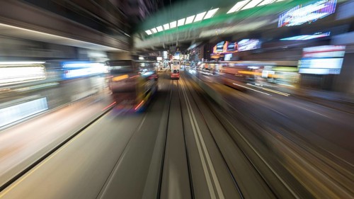 Tarveling through night Hong Kong by double-decker tram. View to road with moving bud and rails
