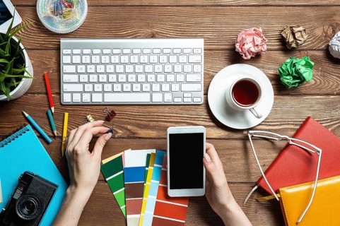 Web designer choosing colors from swatches at wooden desk. Top view office workplace with computer
