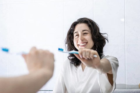 Portrait of a pretty young latin girl holding a toothbrush and smiling in front of the mirror.