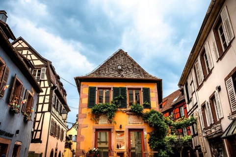 Characteristic half-timbered house with colourful shutters and floral decorations under a cloudy