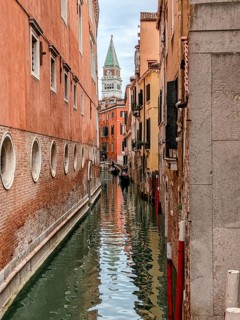 Narrow Venetian canal flanked by historic buildings with the bell tower in the distance. Venice,