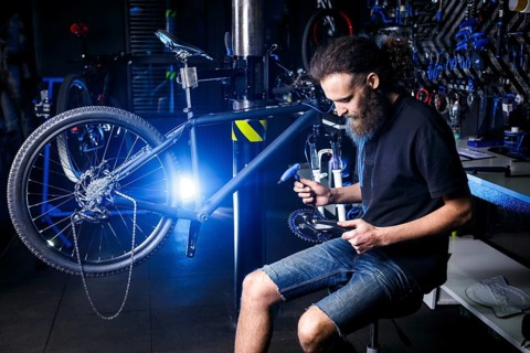 Young stylish bearded, with long hair Caucasian male mechanic worker at a bicycle workshop uses a
