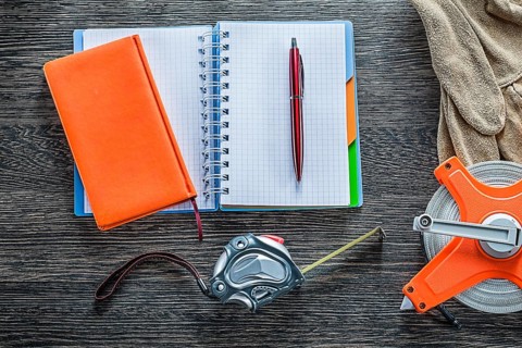 Rolled tape measures safety gloves notebooks pen on wooden board