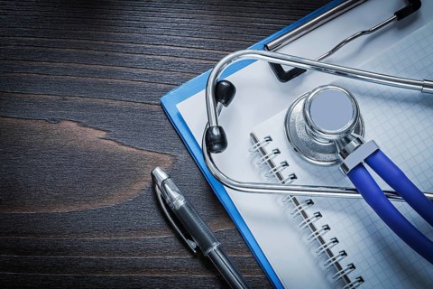Clip board squared notepad pen and medical stethoscope tablet on vintage wooden background medicine
