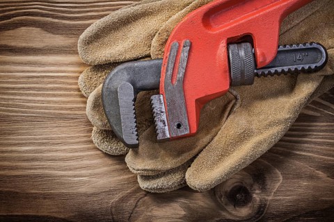 Pair of leather protective gloves pipe wrench on wooden board construction concept