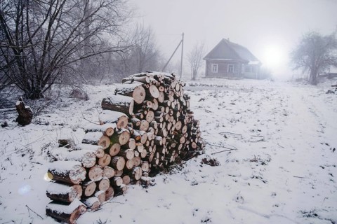 Snowy landscape with a cabin and stacked firewood, depicting a cold rural winter scene