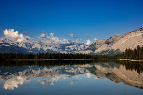 The Canadian Rockies and bright blue sky are reflected in a lake near Canmore, Alberta, Canada,