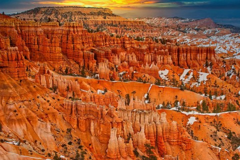 Wide view of a canyon with orange-coloured rocks and snow-covered slopes at sunrise, Bryce Canyon,