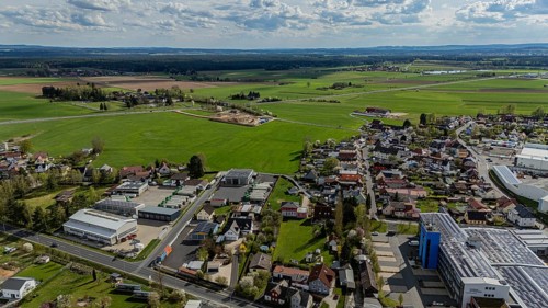 Aerial view of a village with surrounding fields and country road under a cloudy sky, Mitterteich,