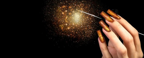 Hand with gold manicure and a brush on a black background covered with sparkles. Nail design.