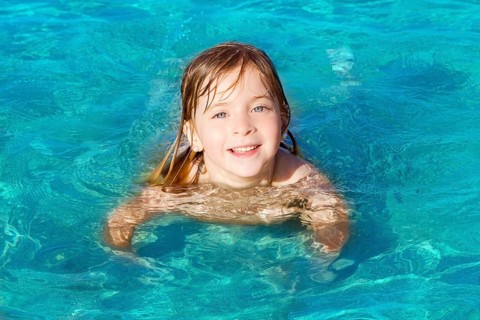 Blond little girl swimming on turquoise beach in Ibiza