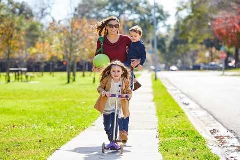 Mother daughter and son family in the park walking with ball and skate scooter