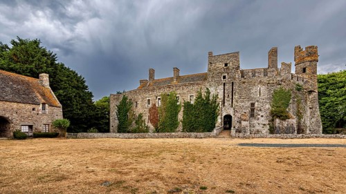 Expansive view of a castle with ivy and a cloudy sky, Pirou Castle in Normandy, France