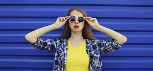 Portrait of modern stylish young woman in white glasses, casual clothing posing on blue wall