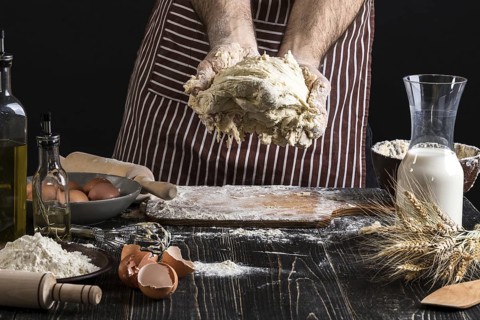 A handful of flour with egg on a rustic kitchen. Against the background of men's hands knead the