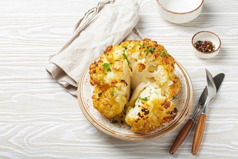 Whole roasted head of cauliflower with olive oil on plate on white wooden rustic table top view
