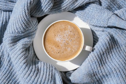 White cup of morning coffee on blue sweater background. Cozy home autumn concept. Aesthetics blog