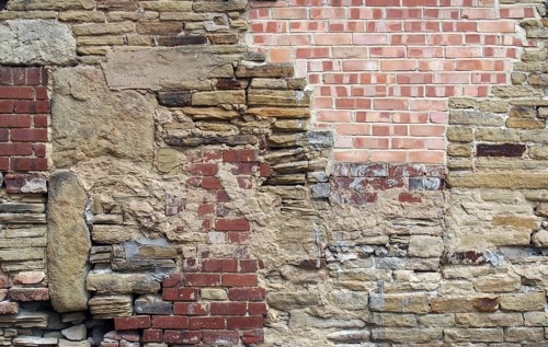 A large old wall made of mixed bricks and stone with many jumbled patched and uneven repairs