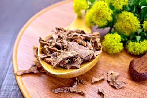 Spoon with dry roots of Rhodiola rosea, knife, fresh flowers Rhodiola rosea on a wooden tray on a