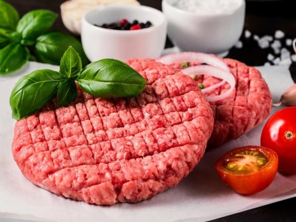 Close up view of two raw meat steak cutlets for burger with vegetables, spices and fresh basil.
