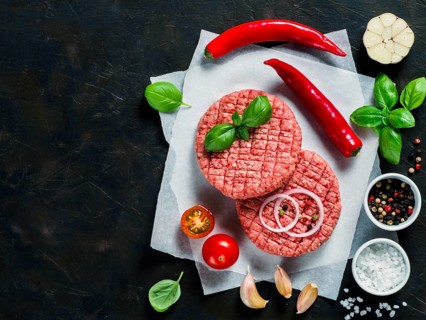 Two raw beef meat steak cutlets for burger with spices and vegetables on black concrete background.