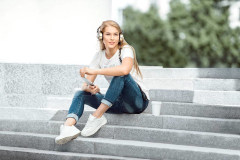 Happy young woman with vintage headphones and a cup of coffee to go, surfing the internet on a