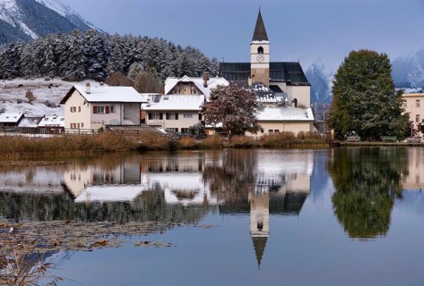 The church in the village Tarasp reflecting in the Taraspsee in the Swiss community Scuol in the