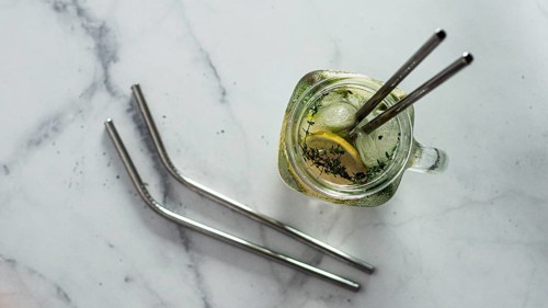 Metal drinking straws and cold drink in glass mason jar on white marble background. Top view or