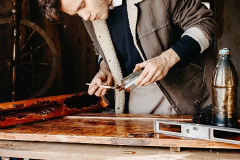 Man applying varnish to wood with precision in a rustic workshop