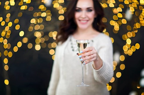 Smiling woman in the sweater with glass of champagne over lights background. Party, drinks,
