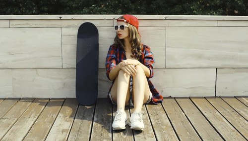 Stylish young woman sitting with skateboard in casual clothes looking away, modern teenage girl