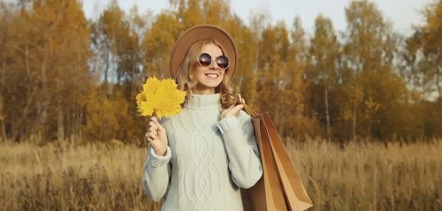 Autumn portrait of stylish happy young woman with shopping bag and maple yellow leaves, fashionable