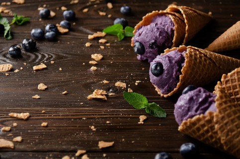 Wafer cones with blackberry icecream on wooden kitchen table with crumbs and berries aside