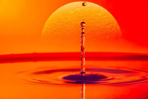 A single drop of water falling into a body of water with a glowing sunset in the background,