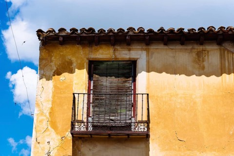 Old Iron Balcony in Aged Yellow Plaster Facade. Old abandoned house