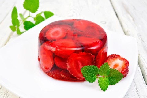 Strawberry jelly with mint and berries in a plate on a kitchen towel on the background light wooden