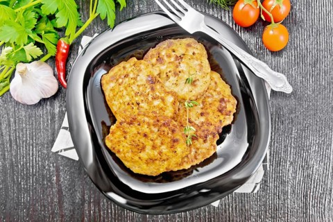 Fritters of minced meat in a plate with a fork on napkin, garlic, parsley and hot pepper on black