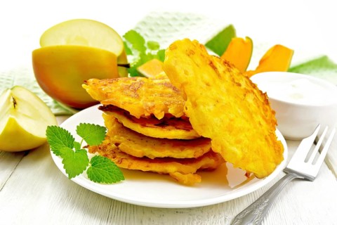 Pumpkin and apple fritters in a white plate, sour cream in a bowl, napkin, mint and fork on wooden