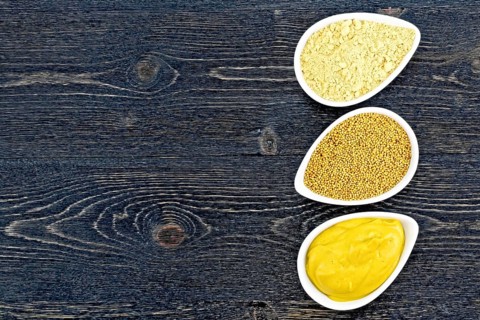 Mustard sauce, seeds and mustard powder in three saucepans on the background of a black wooden
