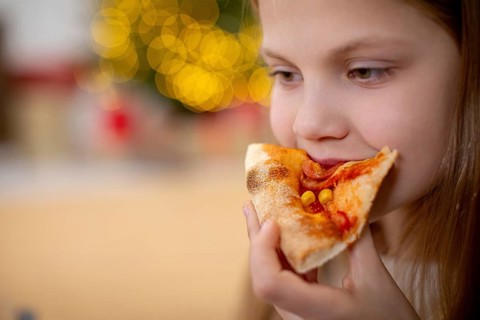 A joyful young child savoring a deliciously tasty slice of pizza, filled with pure happiness in a