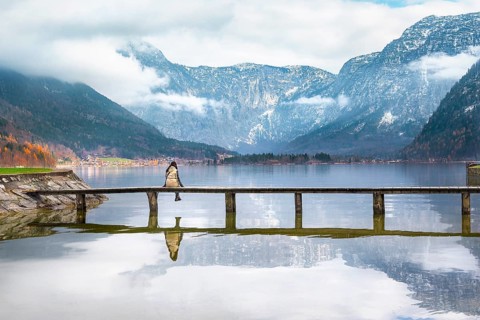 Woman sitting on a wooden bridge over the lake Hallstatter, admiring the peaks of the Austrian Alps