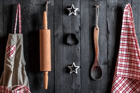 Apron and other kitchen tools hanged with nails on a black wooden wall