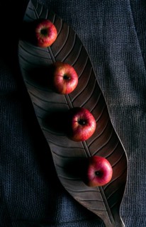 Red apples on a wooden tray in shape of a leaf, on a jute sack, in low light, above view