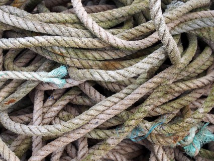 Old worn brown coiled and knotted marine fishing rope with frayed ends stained by the sea