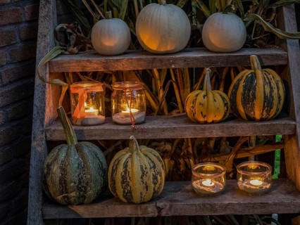 White and yellow striped pumpkins and illuminated candles on a wooden shelf create a cosy Halloween